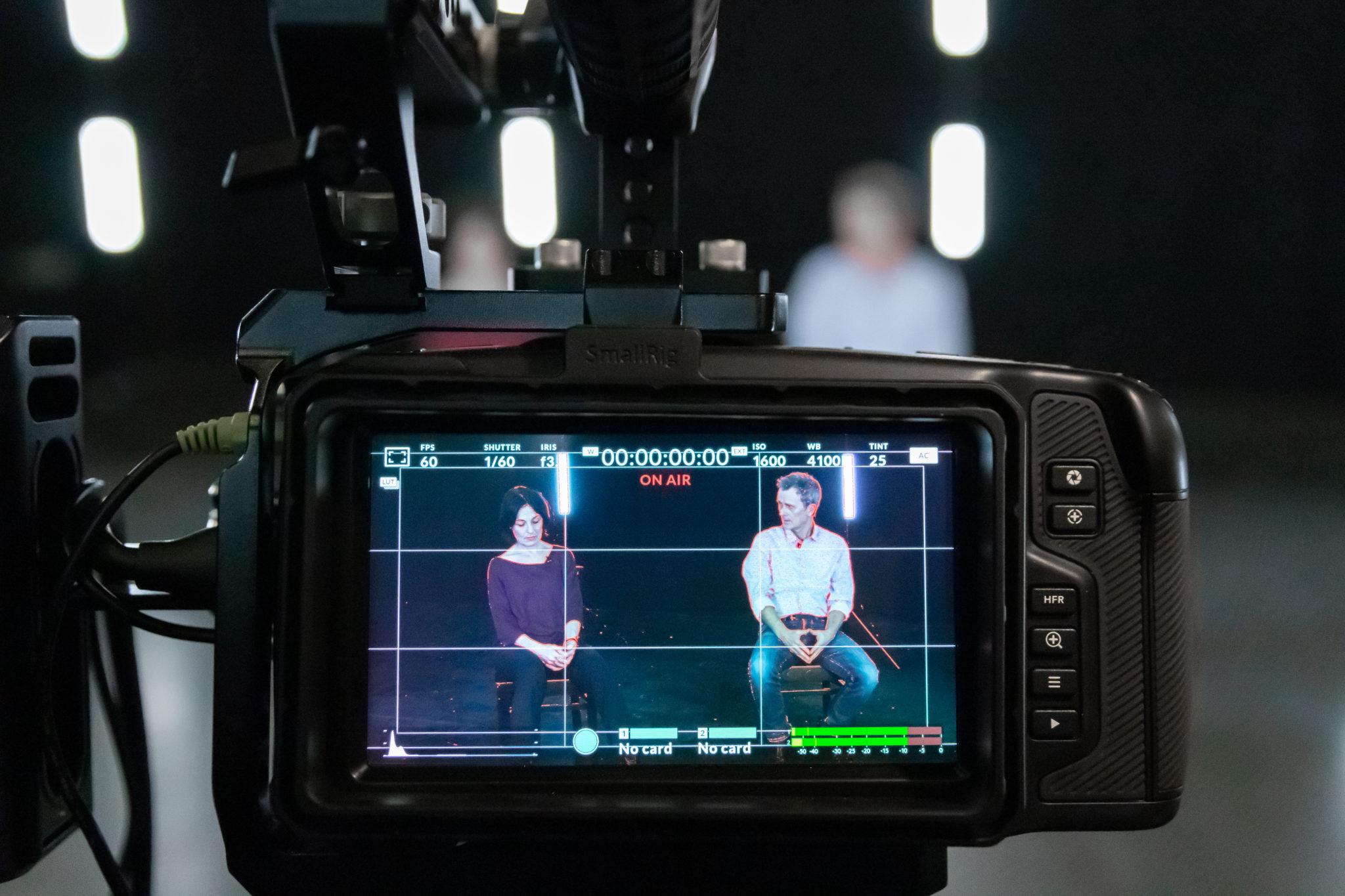 Ein Close Up einer Broadcast Kamera. Auf dem Display sind zwei Schauspieler sitzend zu sehen. Im Display steht neben vielen anderen Informationen in rot "On Air".